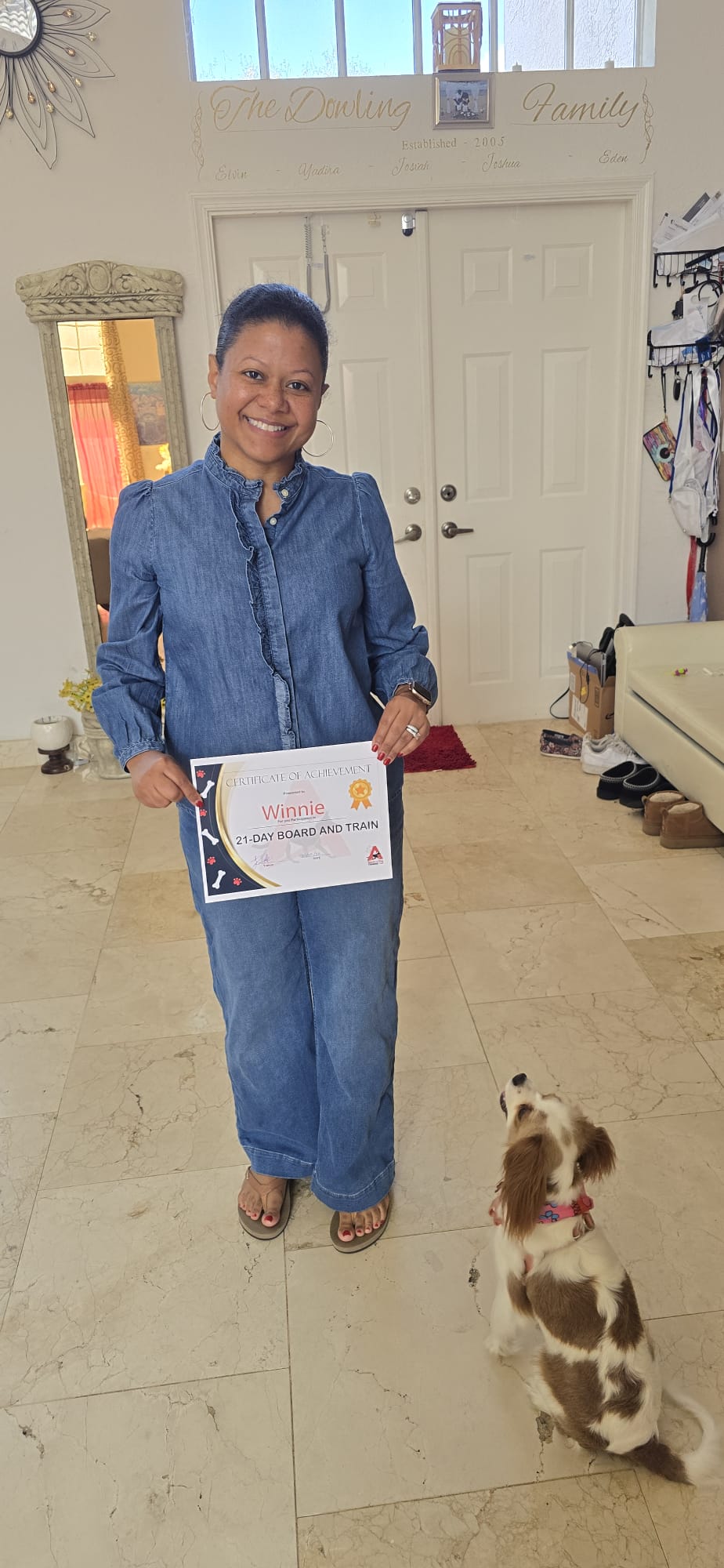 A client holding Winnie's 21-Day Board and Train certificate while her spaniel looks up attentively.