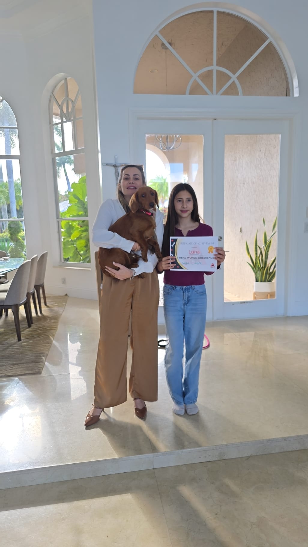 A mother and daughter holding Luna's Real World Obedience certificate with their dachshund.