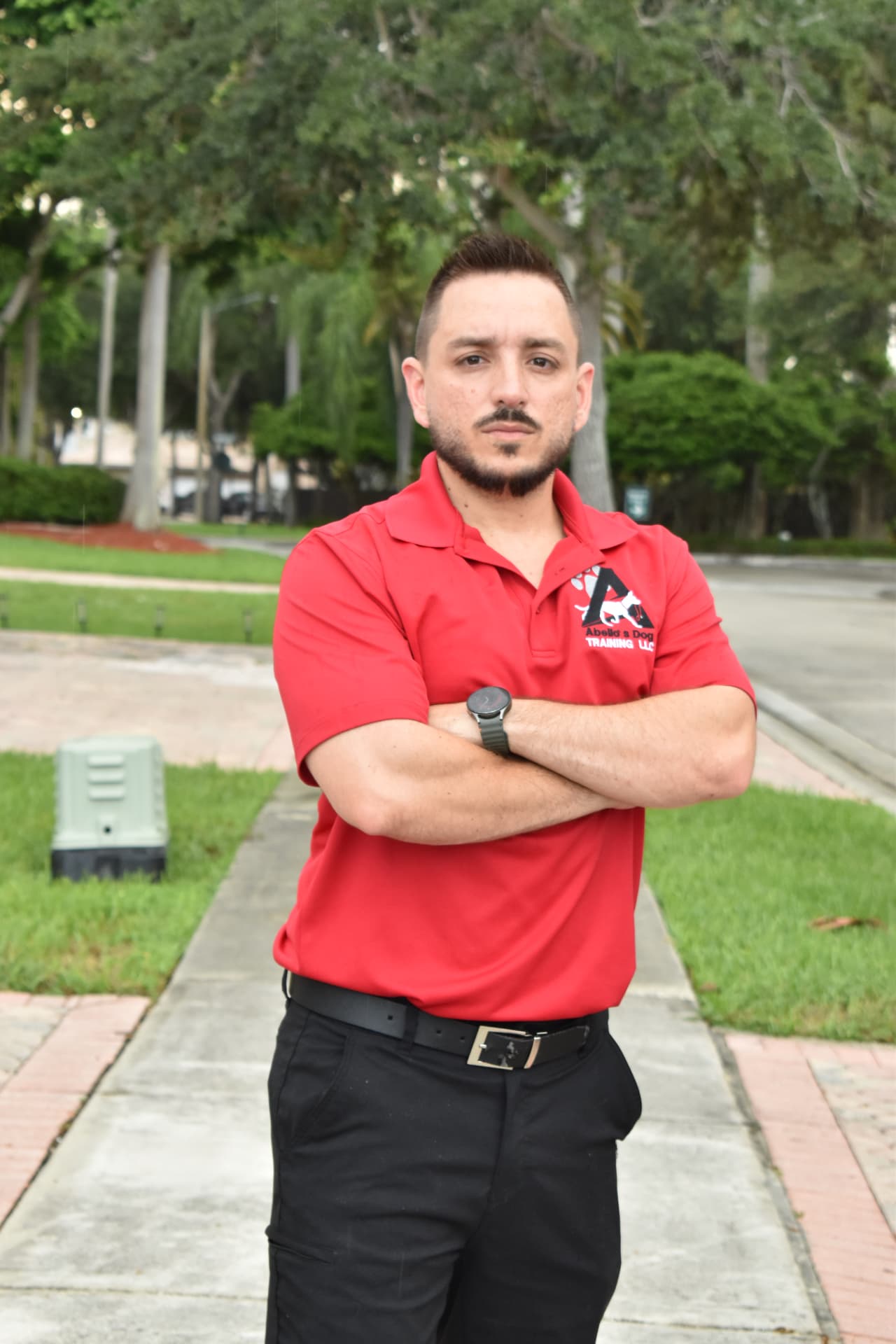 Juan José Abello, founder and head trainer at Abello's Dog Training, standing outdoors in a branded polo shirt.