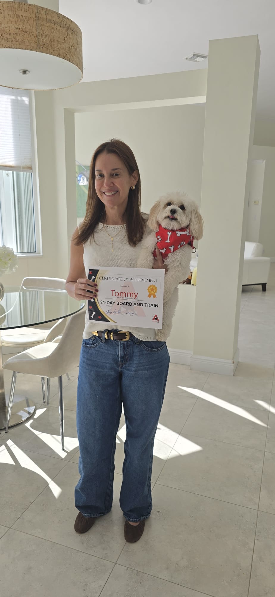 A client holding her small white dog Tommy along with his 21-Day Board and Train certificate.