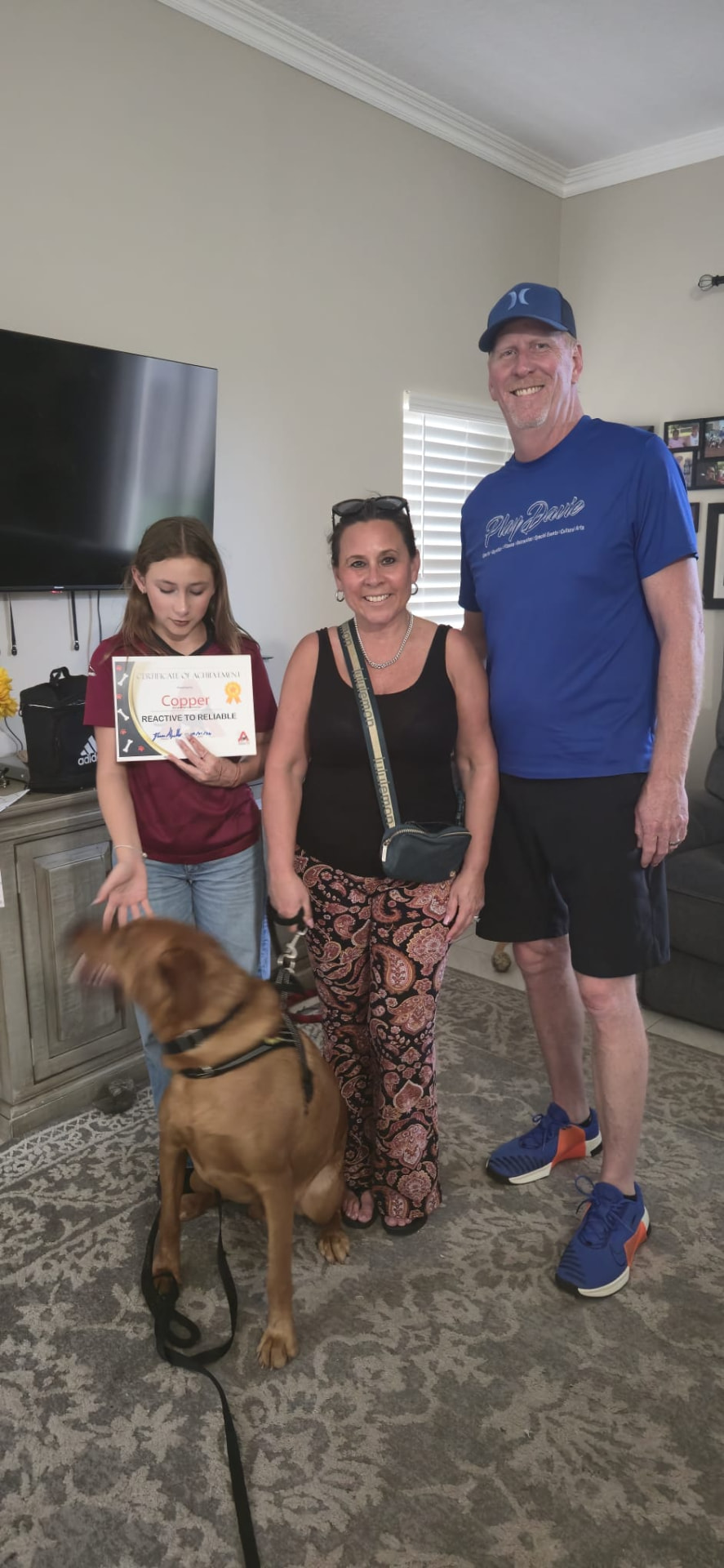 A family holding Copper's Reactive to Reliable certificate with their dog on leash beside them.